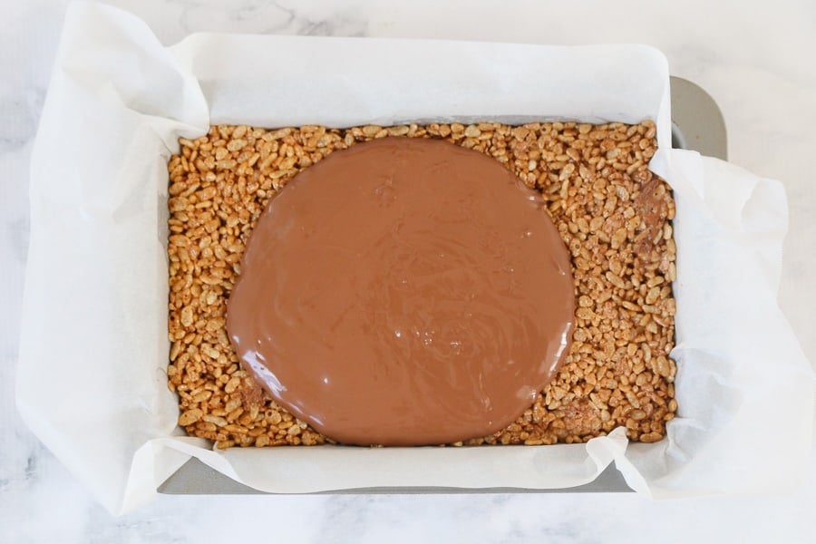 Melted milk chocolate being poured on top of a chocolate rice bubble base. 