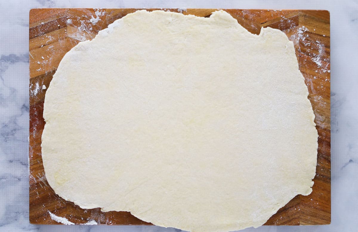 Dough rolled out on a wooden chopping board.